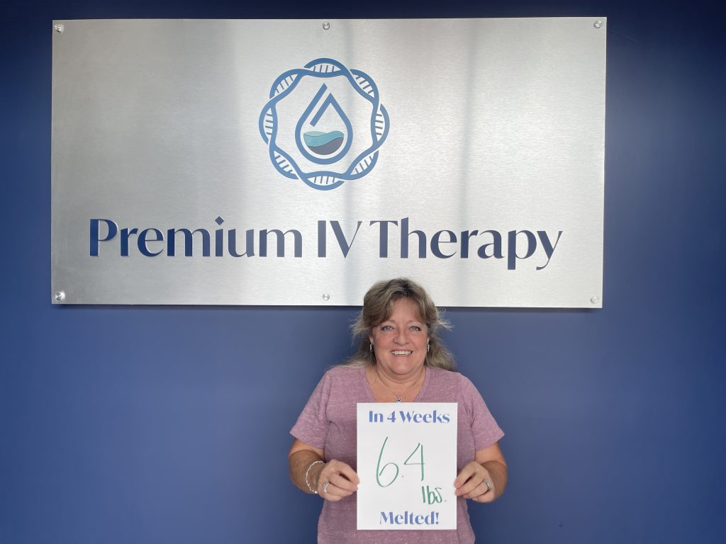 Woman holding a paper with "In 4 weeks 64lbs melted" words on it. behind her is the logo of premium Iv Therapy